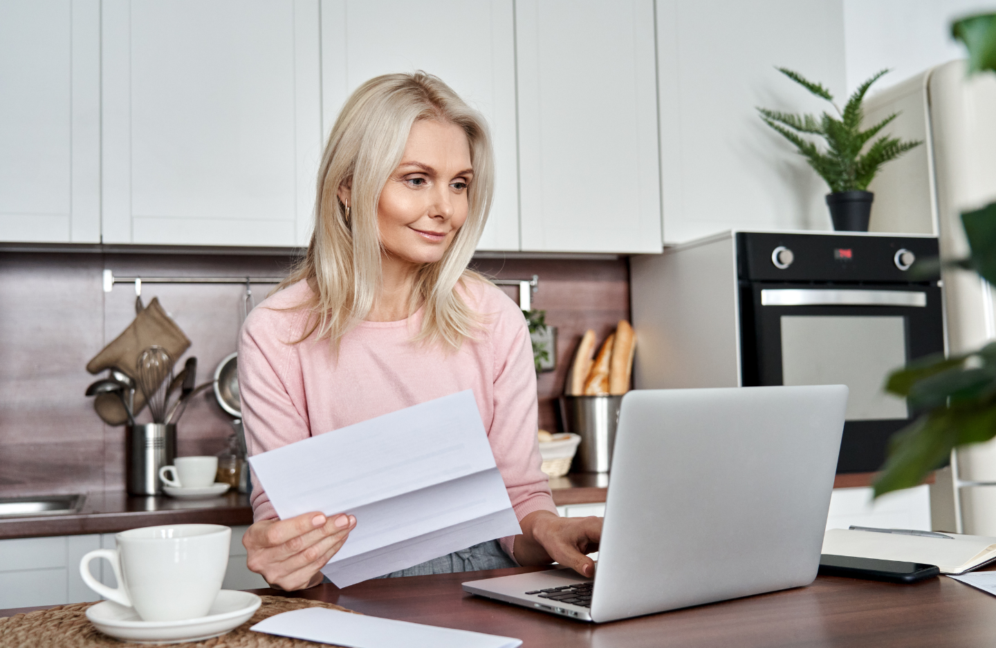 Woman sitting at counter looking at paper and laptop.