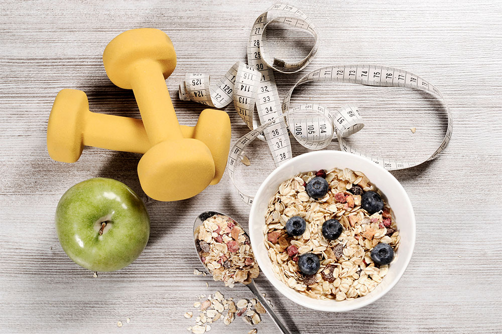oats in a bowl, hand weights, an apple and measuring tape on a table